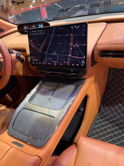 The image shows the interior of a car, likely an electric vehicle. The car is parked, and the interior is illuminated. The center console is brown leather, with a black panel that contains a large touch screen display. The display is showing a map with a variety of icons, indicating that it is a navigation system. Below the display, there is a large, rectangular, black panel with a slight metallic sheen. The panel has a small, rectangular opening in the center, and the edge of the panel is lined with a thin, silver trim. To the right of the panel is a small, black button labeled "TIGHTEN", and a black mat covers the floor. The coordinates provided indicate that this image was likely taken in Hangzhou, China.