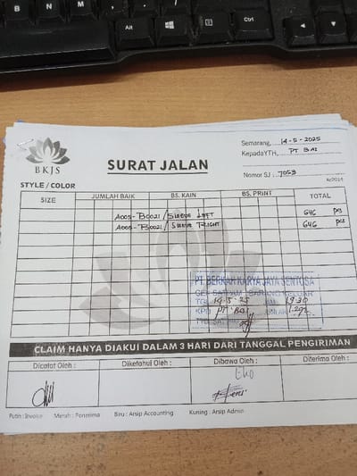 The image shows a "Surat Jalan" (delivery note) form. It is titled "SURAT JALAN" and contains information about a shipment. The document is printed on white paper and filled out in black ink. The delivery note was made on 14-5-2025. It is from "BKJS" and the recipient is "KepadaYTH, PT BAT". The "Nomor SJ" (delivery note number) is 7053. It contains a grid table, with columns labeled "SIZE", "JUMLAH BAIK", "BS. KAIN", "BS. PRINT", and "TOTAL". It lists the size of an item, the number of the item, and the quantity of fabric and print used for each. In the "BS. KAIN" column, the following items are listed: "A005-B0021 / Sleeve Left" and "A005-B0021 / Sleeve Right". Below the grid table, there is a stamp with text in Indonesian that says "PT. BERNIAGA KARYA JAYA SENTOSA" and "CEK SATUAN BARANG KELUAR". The stamp includes details about the date, time, and number of items, with the text "TGL 14-5-25", "JAM 19.30", "KPD PT BAT", and "JUMLAH 1.291." Below the stamp, there is another statement in Indonesian that reads "CLAIM HANYA DIAKU DALAM 3 HARI DARI TANGGAL PENGIRIMAN" (Claim is only recognized within 3 days from the shipment date). Below that, there are four boxes with labels "Dicatat Oleh", "Diketahui Oleh", "Dibawa Oleh", and "Diterima Oleh". The box "Dicatat Oleh" contains a handwritten signature, the box "Diketahui Oleh" is empty, the box "Dibawa Oleh" contains a handwritten signature, and the box "Diterima Oleh" is empty. Below the boxes, there is a note indicating what the colors "Putih", "Merah", "Biru", and "Kuning" represent. "Putih" is marked for "Invoice", "Merah" is marked for "Penerima", "Biru" is marked for "Arsip Accounting", and "Kuning" is marked for "Arsip Admin". The coordinates -7.01, 110.364 correspond to a location in the city of Semarang, Indonesia, which is the likely location where this delivery note was created. The document is likely from a textile factory in Kecamatan Ngaliyan, Semarang, Indonesia.