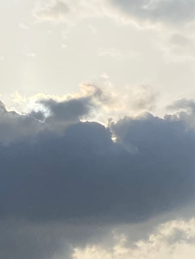 The image depicts a section of the sky with clouds. On the left side of the frame, the clouds are bright white, suggesting sunlight illumination. Adjacent to these, a large, dark gray cloud formation occupies a significant portion of the right side of the image. The edge where the bright and dark clouds meet is highlighted by refracted light. The location of the image is unknown.