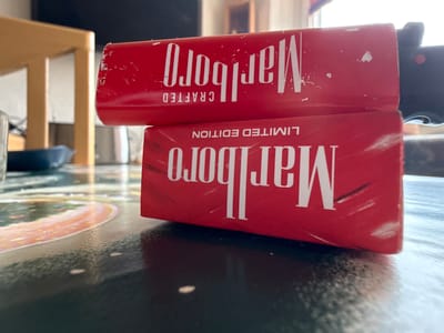 The image shows two packs of Marlboro cigarettes resting against the underside of a table. The top pack is labeled "LIMITED EDITION" and the bottom pack is labeled "CRAFTED." The scene is indoors, with parts of furniture visible in the background. There is no indication of the location being Lüneburg, Germany.