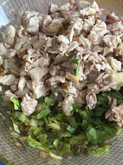 A close-up, overhead shot reveals a dish or ingredients in a clear, textured container, likely a bowl, with a grid pattern visible on its surface. The contents are divided into two main sections.

On the left side, there is a large pile of finely chopped, cooked meat, which appears light-colored, suggesting it might be chicken or pork. Some pieces show brown edges, possibly from skin or slight browning during cooking. The texture of the meat looks tender and somewhat shredded.

On the right side of the container, there is a mix of chopped green leafy vegetables. This includes both finely minced greens, possibly cilantro or parsley, and larger, lighter green pieces that resemble chopped lettuce or cabbage.

The image captures a moment during food preparation or presents a component of a meal, such as a salad or a filling. The lighting is even, suggesting an indoor setting. There are no people visible, no discernible text, and no specific time of day or location cues within the image itself to indicate Egkomi Lefkosias, Cyprus.
