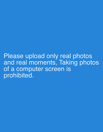 The image displays white sans-serif text centered on a solid blue digital background. The text reads: "Please upload only real photos and real moments, Taking photos of a computer screen is prohibited." No individuals, physical objects, or discernible actions or interactions are depicted within the visual frame. The environment is an undifferentiated, uniform blue digital screen. This digital message is observed within the context of the city of Erba, Italy.
