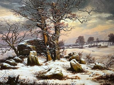 This detailed painting depicts a winter landscape in the city of Reus, Spain. The scene features a snow-covered field under a cloudy sky that transitions from dark grey at the top to hues of orange and yellow near the horizon. In the foreground, numerous large, irregular boulders and rocks are partially covered with snow and moss, interspersed with patches of dry, brown vegetation and sparse bare bushes. Several black birds, appearing to be crows or ravens, are positioned on the snowy ground and atop some rocks. Two tree stumps are visible in the lower left. The mid-ground is dominated by large, bare deciduous trees, likely oaks, with snow accumulating on their complex network of branches; some trees retain a scattering of reddish-brown leaves. In the distant background, rolling snow-covered hills are dotted with bare trees. On the far right, a small, rustic single-story house with a prominent chimney stands in the snow. A lone human figure, accompanied by a small object or animal, is visible walking across the distant snowy field towards the right.