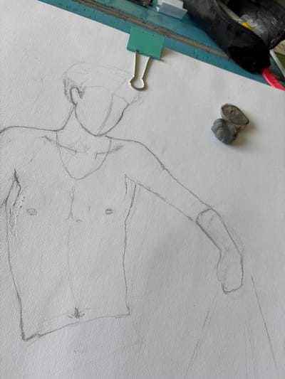 A pencil sketch of a reclining figure is on textured white paper. A kneaded eraser sits above the figure's extended arm. To the left of the paper is a teal surface with a black bag, a red object, and a green binder clip. The city of Troyan, Bulgaria, is not discernible from the image.