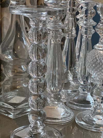 A close-up shot features multiple transparent glass objects with intricate designs, likely the stems of glasses or decorative items. The objects are arranged overlapping each other, creating a complex pattern of reflections and refractions. Some items have spherical or bulbous elements, while others are more elongated and textured. The background is slightly blurred and out of focus, but the overall composition is focused on the details and textures of the glass objects. It is challenging to determine the exact location within Tunbridge Wells without additional information or context.