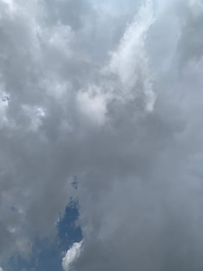 A low-angle, full-frame shot captures a dense, overcast sky with various cloud formations. Dark, ominous clouds dominate the majority of the frame, interspersed with patches of brighter, lighter clouds that suggest breaks in the overcast layer. A sliver of deep blue sky is visible in the lower portion of the image, peeking through the clouds. The scene appears to be a view of the sky from ground level in Barikin Sabon Gidan Kanat, Nigeria. No people, objects, or actions are discernible within the image.