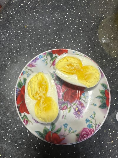 Two halves of a hard-boiled egg, each with two distinct yolks, are presented on a floral-patterned plate. The plate rests on a speckled black countertop. The background is dark and speckled with small white and yellow lights. The image does not contain any information about the city of Karachino, Russia.