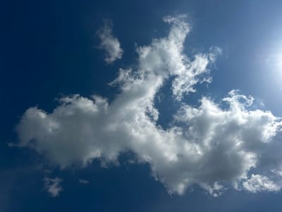A wide-angle shot captures a vibrant blue sky filled with scattered, fluffy white clouds. The sun, partially obscured by clouds, casts a bright glow in the upper right quadrant of the image. The composition is dominated by the natural elements of sky and clouds. This image does not provide any information about the city of Zhlobin, Belarus, or any human presence.