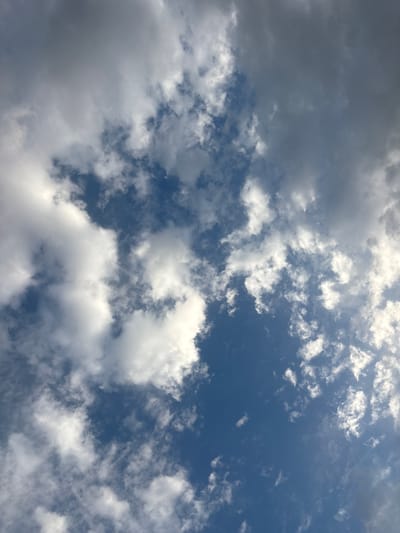 The image shows a sky with varying cloud formations against a blue background. The clouds are a mix of bright white cumulus clouds and darker, grayer stratus clouds, suggesting a partly cloudy day. The perspective is upward, as if looking directly up from ground level. There are no people, objects, or identifiable structures visible in the image, indicating an unobstructed view of the sky. The environment appears to be outdoors, with the sky as the sole subject. There is no specific information that can pinpoint the location to Mārupe, Latvia, or any other specific city.