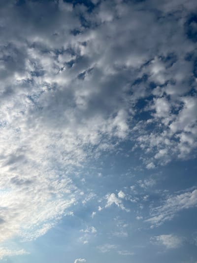 The image displays a sky filled with a mix of dark and light clouds against a blue background. The clouds appear to be in motion, creating a dynamic and textured effect. The lighting suggests it is daytime, with some areas of the sky being brighter than others. The scene is vast and open, with no discernible objects or structures on the ground, implying an outdoor setting, possibly a view from a high vantage point or an open landscape. There is no visible text in the image. The overall mood is natural and serene, with the interplay of light and shadow on the clouds creating a sense of depth and movement.