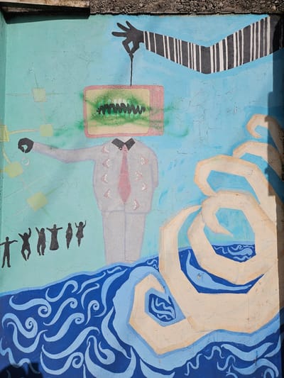 Mural art on a light blue wall in Osorno, Chile. It depicts a stylized scene with an elongated, gray-suited figure lying horizontally in the center. The figure has a pink tie and a series of triangular shapes lining its chest. Above the figure, there is a large, pale-colored hand with outlined fingers. To the right of the figure, there is a blue pattern of swirled lines. Below the figure, there is a row of small, black silhouettes that appear to be human figures in various poses. To the left of the figure, there's a black and white striped pattern and a dark hand holding a line that connects to a green and tan rectangle. Three squares are connected by lines below the suit, towards the bottom of the scene.
