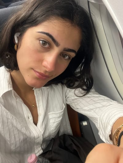 A young woman with dark hair and light skin is lying down, possibly on a plane given the presence of the cabin interior in the upper left. She is wearing a light-colored striped shirt and a gold necklace. She appears to be looking at the camera. The location is likely in the city of Paray-Vieille-Poste, France, given the context provided.