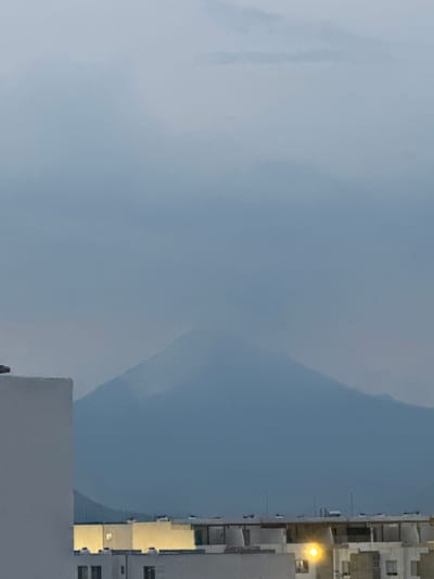 The image shows a view from the city of San Francisco Ocotlán (Ocotlán), Mexico, with a building visible on the right. The building appears to be tall with multiple windows and a light shining from within. The left side of the image is filled with a cloudy or overcast sky. The overall scene appears to be taken during the day, possibly in the early morning or late afternoon.