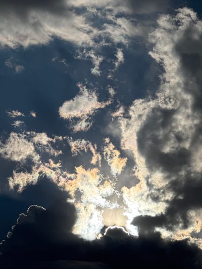 This is a photograph of a cloudy sky, taken from below, looking upwards. The clouds are varied in density and color, with some appearing dark and ominous, while others are brightly lit by the sun, creating a dramatic contrast. The sun is partially obscured by a large, dark cloud formation on the right side of the frame, but its intense brightness can be seen peeking through, casting rays of light that illuminate the edges of other clouds with a golden and iridescent glow.
The clouds exhibit a range of textures, from wispy and thin to thick and voluminous. Some clouds have sharp, defined edges, particularly where the sunlight catches them, while others appear softer and more diffused. The sky itself is a deep blue, suggesting it is daytime. There are no people or man-made objects visible in the image, focusing solely on the natural phenomenon of the sky and its atmospheric conditions.
The lighting suggests it might be late afternoon or early evening, as the sun's angle and the intensity of the light create strong shadows and highlights. The overall mood is dramatic and awe-inspiring, with the powerful interplay of light and shadow in the clouds evoking a sense of grandeur and the raw power of nature. The location context of Pavlodar, Kazakhstan, does not provide any specific visual cues within the image itself, as the scene is a universal depiction of a cloudy sky. There is no visible text in the image.