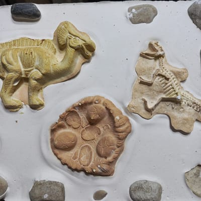 The image depicts a collection of dinosaur fossil replicas embedded in a white, artificial substrate.

*   **Subjects**: Replicas of a Parasaurolophus, a theropod skeleton, and a dinosaur footprint are the central subjects.
*   **Objects**: The replicas are surrounded by small, natural pebbles of varying colors (grey, brown).
*   **Environment**: The white substrate appears to be a man-made material, possibly plaster or a similar compound.

There is no information to establish that this image is related to the city of Guayaquil, Ecuador. No people are visible, so information concerning their actions and interactions is not available.