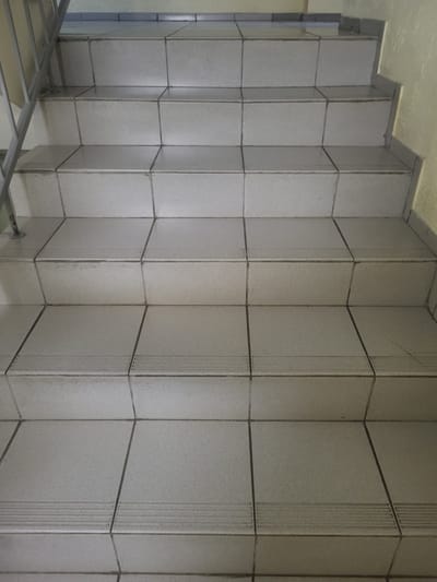 The image shows an indoor staircase with light-colored tiled steps. A metal handrail is visible on the left side of the staircase. The environment appears to be a building, possibly an apartment complex or a public building. There are no people or specific activities depicted in the image. The scene is static and focuses on the architectural details of the staircase. The location of Khotsky, Ukraine, is not visually indicated in the image.