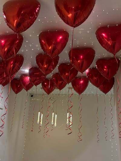 The image shows a room decorated with red, heart-shaped balloons attached to the ceiling with red, curling ribbon. String lights also adorn the ceiling. No people are visible. The location is inferred to be in Neftekamsk, Russia, but no evidence in the image directly supports this location.