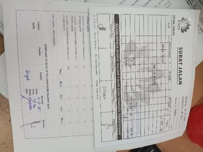 The image is of a partially filled out document in Indonesian. The document's title is "SURAT JALAN", or "Delivery Note", and it appears to be a form for the shipment of goods. It includes a grid where the sizes and colors of the goods can be entered. The document also has a section labeled "ELAINNYA HANYA DIAKUI DALAM 3 HARI DARI TANGGAL PENGIRIMAN", which means "Complaints will only be accepted within 3 days of the date of shipment." The document is signed by a person with the signature "Sugito". The document is lying on a table with a red object in the bottom right corner. The document does not appear to be located in Kecamatan Ngaliyan, Indonesia, based on coordinates (latitude: -7.01, longitude: 110.364).