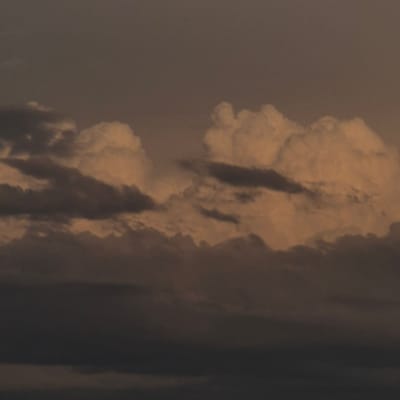This media file depicts a dramatic and turbulent sky, possibly a sky filled with smoke or thick clouds. The main subject appears to be a massive, dark, and billowing plume rising vertically. The plume is illuminated by a warm, orange light from what could be a sunset or sunrise, casting deep shadows and highlighting the textured, swirling nature of the smoke or clouds.
The scene is abstract and somewhat ominous, with the dominant colors being shades of brown, orange, and dark grey. The textures suggest intense atmospheric activity, possibly volcanic eruption or a large-scale fire. The composition is vertical, emphasizing the upward movement and immensity of the plume. There are no discernible people, objects, or specific location cues, other than the provided context of "Novostroyka, Russia." The time of day is suggested by the warm lighting, implying either dawn or dusk. The weather is clearly extreme and dramatic, characterized by the thick, turbulent atmospheric phenomenon. No text is visible in the image.