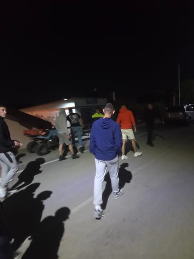 The image shows a group of people on a paved surface that appears to be a road or parking area. The setting is dark, likely nighttime, with lighting coming from streetlights or nearby buildings, as evidenced by the shadows cast by the people.

Several individuals are visible, some lying down, and others standing. One person wears a blue hooded sweatshirt and light-colored pants, another wears a red sweatshirt and light shorts. There is an All Terrain Vehicle(ATV) present. A car is in the background. The image is taken from a low angle.

There is no concrete indication of Pripek, Bulgaria, in the image.