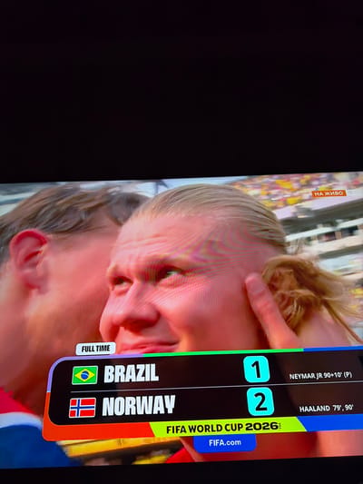 The image is a close-up photograph of a television screen displaying a soccer match scoreboard. The scoreboard shows that Brazil has scored 1 goal and Norway has scored 2 goals. The match appears to be a friendly or exhibition game, as indicated by the "FULL TIME" label and the names of the goal scorers, Neymar Jr. and Haaland. The background of the image shows a crowd in a stadium. The location in the city of Ognianovo, Bulgaria, is not visible in the image.