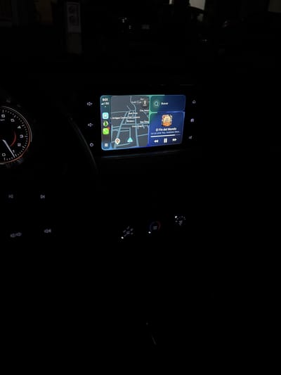 The image shows the interior of a vehicle, focusing on the infotainment system screen. The screen displays a map of San Francisco Ocotlán (Ocotlán), Mexico with navigation and a music player interface. The music player is playing "El Fin del Mundo" by La La Love You, Axolotes Mexicanos. Below the screen is the steering wheel, with only the speedometer visible. The clock on the screen indicates 9:01. The location on the map appears to be at or near "Antiguo Camino San Lorenzo" and "Riviera". The image is taken in a dark environment, with only the screen and some car dashboard lights illuminated.