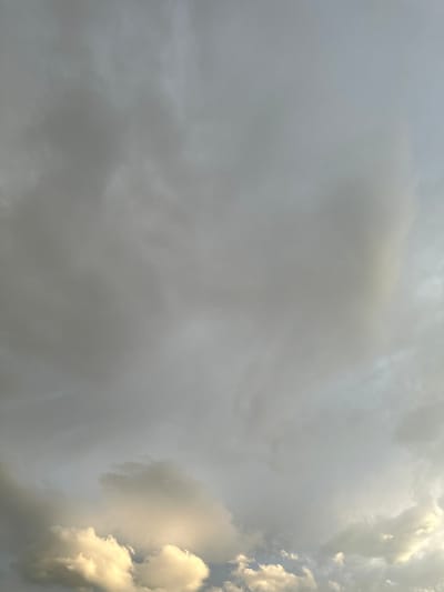 The image shows a cloudy sky with varying shades of gray and white. The clouds appear to be low-lying, and some are illuminated by sunlight, creating brighter patches. The sky occupies the entire frame of the photograph. There are no people, structures, or discernable landscape features visible in the image, only the clouds and sky. The location is specified as Сарымолдаев ауылдық округі, Kazakhstan, however, there are no visual cues in the image to confirm this specific geographical location; it is a purely textual annotation.
