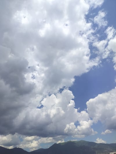 The image depicts a sky filled with a mix of white and gray clouds, with patches of blue sky visible. In the lower portion of the image, a dark, undulating mountain range stretches across the horizon. The scene appears to be a landscape view, likely taken from an elevated position within or near the city of Gorno Sahrane, Bulgaria, given the mountainous terrain. No people or specific structures are clearly identifiable within the frame.