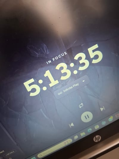 The image displays an angled, close-up view of a digital screen, likely from an HP laptop or tablet, as indicated by the HP logo visible on its bezel. The screen's interface is predominantly dark, featuring large, bright yellow numbers "5:13.35," which appear to be a timer or stopwatch. Below these numbers, smaller white text reads "IN FOCUS," suggesting the use of a productivity or focus-oriented application. To the right, rotated white text states "∞ Infinite Play," accompanied by media control icons including a pause button (two vertical lines), skip forward/backward arrows, and a refresh or loop icon, indicating an ongoing audio or video playback in a continuous mode.

The top edge of the screen shows a partially visible status bar with various icons, such as battery and Wi-Fi indicators, along with several application shortcuts. At the bottom right, a blurred element with the text "+ DETAILS" is also visible. The screen surface exhibits reflections and smudges, typical of a device in use indoors. While the image itself lacks specific location cues, it is contextually placed in Naucalpan de Juárez, Mexico.