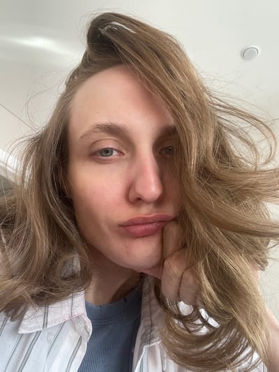 A close-up, rotated view depicts a fair-skinned person with light brown hair, wearing a light blue top under a white and gray striped shirt. Their face is positioned prominently, with their hand compressing their cheek. The background is white, with a circular white fixture visible in the upper left corner. The image provides no discernible information to identify a specific location or indicate it was taken in the city of Sepych, Russia.