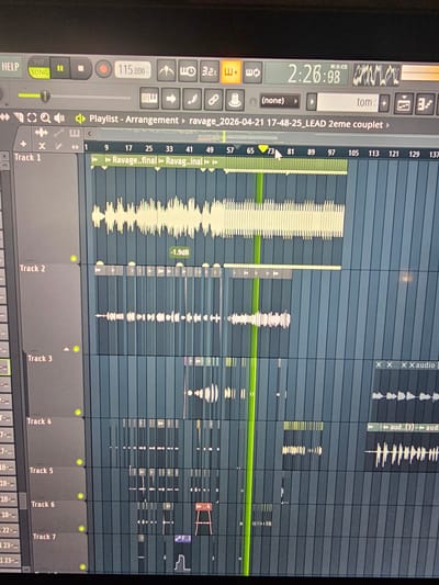 A slightly rotated, close-up photograph captures a computer screen displaying music production software, identifiable as FL Studio. The primary activity shown is audio editing and arrangement within the software's playlist view.

The interface reveals an active music project named "ravage_2026-04-21 17-48-25_LEAD 2eme couplet," suggesting a track titled "ravage" with a lead part for a "second verse." A green vertical line indicates the current playback position, approximately at bar 73 on the timeline. Various audio clips, represented by waveforms, are arranged across multiple tracks. One prominent clip on "Track 1" is labeled "Ravage..final" and shows a volume adjustment of "-1.9dB." Other visible clips are labeled "Ravag..inal," "X audio," and "aud...(3)."

The top left of the screen shows a timer displaying "2:26:08" (Minutes:Seconds:Centiseconds) and a tempo setting of "115.000" BPM. Control elements like play, pause, record, loop, and metronome buttons are visible, along with a volume slider for the master track. Tracks 1 through 7 are visible at the bottom of the playlist, each with a green indicator light, suggesting they are active or enabled. The overall scene depicts a digital audio workstation in active use, likely by a music producer or sound engineer in Pantin, France.