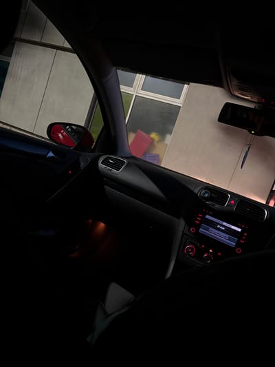 The image shows the interior of a vehicle. The dashboard and infotainment system are visible. Through the windows, the exterior environment appears to be a parking garage or industrial building. There are no people visible. The precise location within Leicester, United Kingdom, cannot be determined from the given image.