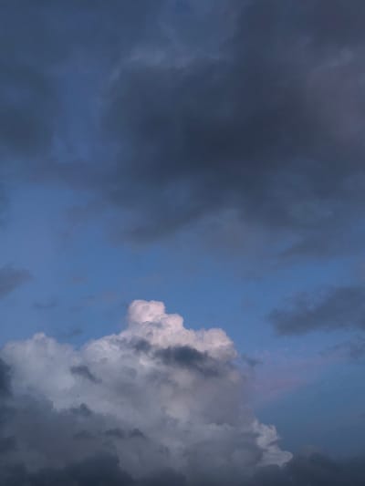 A low-angle shot captures a dramatic sky filled with dark, ominous storm clouds. The upper portion of the image is dominated by deep blues and grays, indicating heavy cloud cover. Towards the bottom, a massive, luminous cumulus cloud stands out, illuminated from within by soft pink and white light, contrasting sharply with the darker clouds surrounding it. The overall impression is one of an approaching or passing storm. The location is specified as Thiththagalla, Sri Lanka, suggesting a tropical environment where such dramatic weather patterns are common. No people, animals, or man-made structures are visible. The scene is static, focusing solely on the atmospheric conditions.