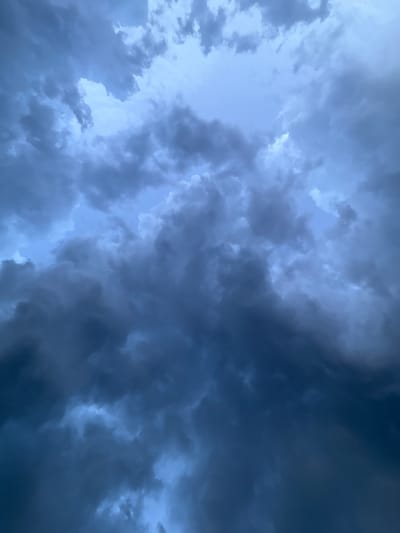 The image depicts a dramatic sky filled with dark, ominous storm clouds. The clouds are dense and turbulent, with varying shades of gray and deep blue, suggesting an impending storm. Patches of lighter sky peek through, creating a sense of depth and contrast. The perspective is looking upwards, emphasizing the immensity and power of the clouds. There are no people or objects visible, making the sky the sole subject. The overall mood is one of intensity and anticipation, likely evoked by the approaching weather. The image captures a moment of natural drama, with the clouds swirling and gathering in a powerful display. The lighting suggests it could be late afternoon or early evening, or simply a very overcast day. While no specific location cues are visible within the frame itself, the provided context places the scene in Baan Chaweng Noi, Thailand. The weather appears stormy or about to become stormy.