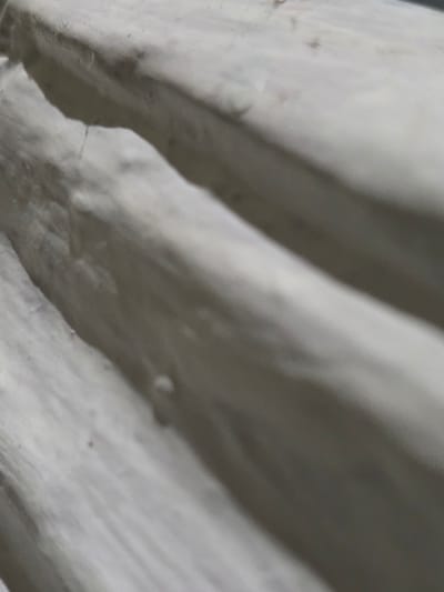 The image shows a close-up, abstract view of textured, off-white material, possibly fabric or a soft, pliable substance. The lighting creates shadows that highlight the contours and ridges of the material, giving it a three-dimensional appearance. There are no identifiable landmarks or elements that would allow for the determination of a specific location within Bireuenmeunasahblang, Indonesia. The scene is devoid of people, actions, or interactions, focusing solely on the texture and form of the material.