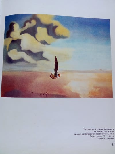 The image is a painting that depicts a surreal landscape with a single boat on a beach. The sky is filled with dramatic, swirling clouds in shades of yellow, white, and dark gray, contrasting with a pale blue sky. The beach appears vast and sandy, with a gradient of colors from reddish-brown in the foreground to lighter sandy tones in the distance, reflecting the sky.

In the middle ground, a small, wooden boat with a tall, dark, conical sail is present. A figure, possibly a person, in white clothing can be seen in the boat. The boat is positioned on the wet sand near the water's edge. In the far distance, a faint landmass or horizon line is visible. In the lower left foreground, there are several small, dark bird-like figures in flight.

Below the painting, text in Russian provides details about the artwork. The title translates to "The Apparition of My Cousin Caroline Henriette on the Shore of Port Lligat (a slowly advancing presentiment), 1933." The medium is specified as "Canvas, oil; 73 × 100 cm." and the collection as "Private collection."

The painting is not located in Zhmerynka, Ukraine. The text indicates the artist likely depicted a scene in Port Lligat, Spain.