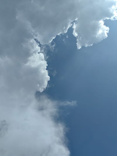A low-angle, full outdoor shot features a sky filled with clouds and blue sky. The clouds are predominantly white with gray undersides, with some appearing wispy and others more dense. The blue sky is visible in the right half of the frame, with a gradient from a lighter shade near the horizon to a deeper blue at the top. The clouds are gathered on the left side of the image, creating a dramatic contrast with the clear sky. The scene is devoid of any human presence or man-made structures, suggesting an open, natural environment, possibly a landscape in Krestovo-Gorodishche, Russia.