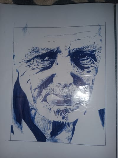 This is a close-up, eye-level, medium shot of a blue ink sketch of an elderly man's face. The sketch is rendered in a rough, expressive style, with heavy lines used to define features and shading. The man's face is deeply lined, suggesting age and perhaps a life of hardship or experience. His eyes are shadowed, and his mouth is set in a neutral expression. The sketch is framed by a thin black border. The lighting in the image creates a significant glare on the surface of the sketch, obscuring some of the finer details. The background is blurred and indistinct. There is no visible text. The context provided is Gulbag, Uzbekistan.