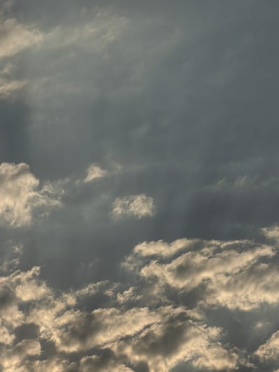 The image depicts a dense, overcast sky with varying shades of grey and illuminated clouds. The lower portion of the image shows a thick layer of cumulus clouds catching the light from below, creating a dramatic contrast with the darker, more diffuse clouds above. There are no people, structures, or specific landmarks visible that would indicate a location within Chirchik, Uzbekistan. The scene is solely focused on the atmospheric conditions of the sky.
