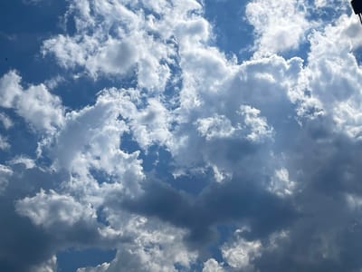 The image shows a cloudy blue sky. There are several fluffy white clouds scattered across the sky, with some darker, more ominous clouds in the lower portion of the frame. The image appears to be taken from an outdoor perspective, looking upwards. There is no visible indication of the city of Berkovitsa, Bulgaria, or any specific geographical features. The scene is devoid of any people, subjects, objects, or actions. The environment is solely the sky with clouds.