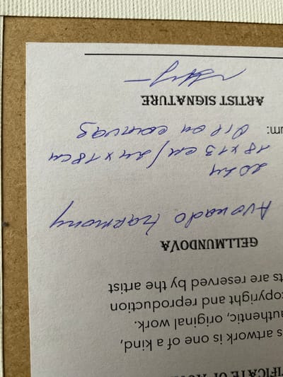 The image shows a close-up of a white certificate with a textured cream-colored border. The certificate is partially mounted on a brown backing board. Text is printed and handwritten on the certificate.
Printed text includes "ARTIST SIGNATURE" and the name "GELLMUNDOVA" in a stylized font. There is also a block of text at the bottom which is partially visible and reads "s artwork is one of a kind, authentic, original work. copyrignt and reproduction rights are reserved by the artist".
Handwritten text in blue ink is present. At the top, there is a stylized signature. Below "ARTIST SIGNATURE", there is handwritten text. The first line appears to be "2024". The second line is "18 x 13 cm / 18x18cm". The third line appears to be "oil on canvas". The fourth line reads "Auevado Harmony".
The image does not provide any information about the city of Bílina, Czechia. The image focuses solely on the document itself.