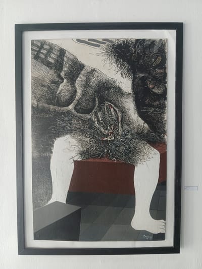 The image shows a framed artwork hanging on a white wall. The artwork features a combination of drawing and painting. The left side has a black and white drawing with dense, scribbled lines depicting what appears to be a distorted face or skull with cavernous eye sockets. On the right side, the artwork incorporates painted elements. Two white legs, seemingly disconnected from a torso, are painted against a background of geometric shapes in shades of brown and gray. The artwork is signed "Henrique 86" on the lower right side near the foot. The image appears to be taken in an art gallery or similar setting in Guayana City, Venezuela.