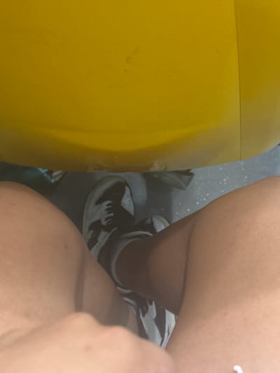 The image shows a low-angle perspective of a person's legs and feet, wearing dark sneakers and socks. A large, curved yellow object dominates the top portion of the frame, casting a shadow below. The background appears to be a dark, textured surface, possibly flooring, with some scattered white specks. The lighting is uneven, with a strong light source likely coming from above. The overall scene suggests an indoor environment, possibly a public space or a recreational facility. The location within l'Hospitalet de Llobregat, Spain, cannot be determined from the visual information alone.