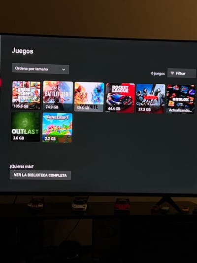 The image displays a screen showing a list of video games. The games are sorted by size, from largest to smallest. The largest game is "Grand Theft Auto" at 105.6 GB, followed by "Battlefield 1" at 74.9 GB, "Fortnite" at 59.6 GB, "Rocket League" at 44.4 GB, "Siege" at 37.3 GB, "Outlast" at 3.6 GB, "Minecraft" at 2.2 GB, and finally "Roblox" which is currently updating. The interface is in Spanish, with options to filter the list and view the full library. The screen appears to be a television or monitor, and the photo was taken indoors. There is no indication that this image is located in Arroyo Hondo, Mexico.