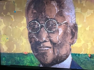 The image is a close-up, slightly blurry photograph of a television screen displaying a painting. The painting depicts a portrait of a man with glasses, rendered in a mosaic-like style using circular shapes of varying shades of brown and tan. The background of the portrait is a pale yellow, also composed of similar circular shapes. Below the portrait is a band of green, textured to resemble grass or foliage, with a red object resembling a fish or a piece of fruit visible in the lower right quadrant. There is a subtle blue speck visible in the upper left quadrant of the background. The man in the portrait appears to be wearing a dark suit. The image is captured from an angle, indicating it is a photograph of a screen. There is no discernible location in the city of Liverpool, United Kingdom, depicted in the image.
