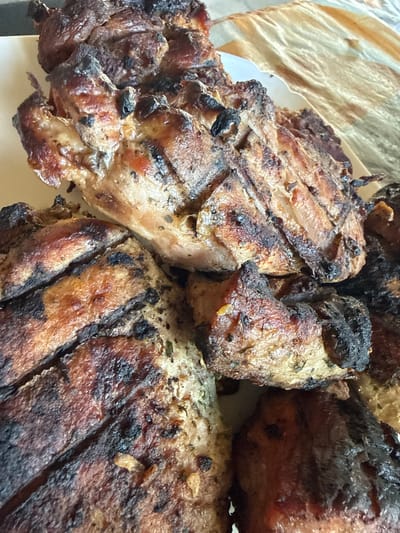 This media file is a close-up, overhead shot of several pieces of grilled meat. The meat appears to be pork, with visible grill marks and some charred edges, indicating it has been cooked over an open flame or grill. The lighting suggests it is daytime, likely outdoors given the grilled food. There are no people, text, or specific environmental cues to suggest a precise location beyond the implied setting of a meal preparation or serving. The focus is entirely on the texture and appearance of the cooked meat.