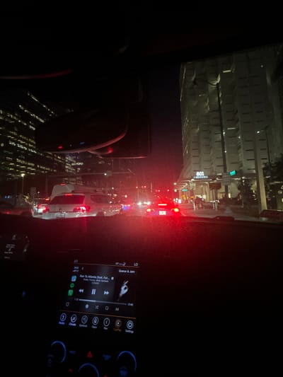This media file captures a scene from inside a vehicle, likely a car, at night in a city. The view is directed forward, showing traffic and the urban environment. The main subjects are the road, other vehicles, and the illuminated buildings lining the street. A digital display, presumably a car's infotainment system, is visible on the right side of the frame, showing song information and controls for media, climate, and navigation. The song displayed is "Ran To Atlanta" by Drake, Future, and Molly Santana, featuring ICEMAN.
Notable details include the time of day being night, indicated by the darkness and artificial lighting. The weather appears to be clear, as there are no visible signs of rain or fog. Location cues suggest an urban setting, with tall buildings and streetlights. The building on the left is marked with "801 SBRICKELL," indicating a specific location in Miami, United States of America. Traffic lights and brake lights of other cars are prominent, suggesting the vehicle is in traffic. The overall mood is typical of a nighttime drive in a bustling city. The focus is on the sensory experience of being in a car at night, with the interplay of artificial lights and the sounds of music.