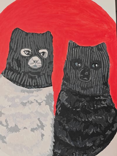 The image is a painting depicting two cats wearing balaclavas against a red circular background. The cat on the left is mostly white with grey and black markings on its face and wears a grey balaclava. The cat on the right is black with grey markings on its face and wears a black balaclava. The painting is in a stylized, somewhat abstract manner. There is no indication of the city of Koledino, Russia, within the image.