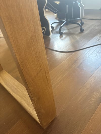 The image shows a close-up view of a wooden table leg and the wooden floor in front of it. In the background, out of focus, is a black office chair with wheels. A black cable runs across the floor. The scene appears to be indoors, likely in a residential or office setting. The location in the city of Orekhovka, Russia is not discernible from the visual information provided in the image.