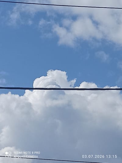 The image depicts a clear blue sky with scattered white, fluffy clouds. Two black wires traverse the frame horizontally, suggesting an outdoor, possibly urban or suburban, setting. The lower portion of the image shows more dense clouds. In the bottom left corner, a watermark reads "REDMI NOTE 8 PRO AI QUAD CAMERA". In the bottom right corner, a date and time stamp indicates "03.07.2026 13:15". The scene is devoid of people or any specific landmarks that would pinpoint a location within the city of Sovetskiy, Russia.